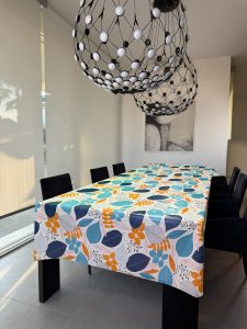 tovaglia con base bianca e stampe di foglie blu e azzurre e rami arancioni